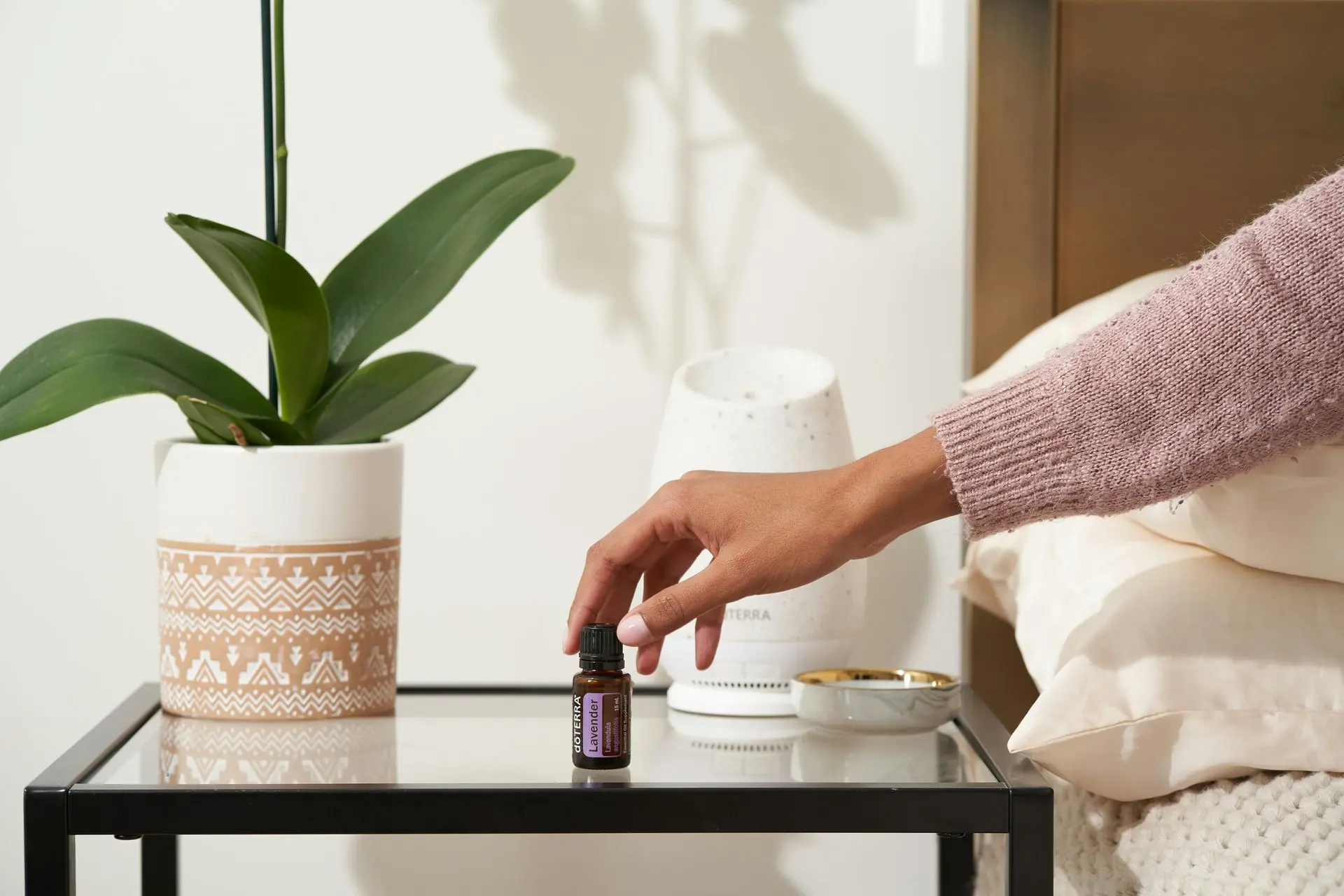 Hand placing essential oil near diffuser on side table.