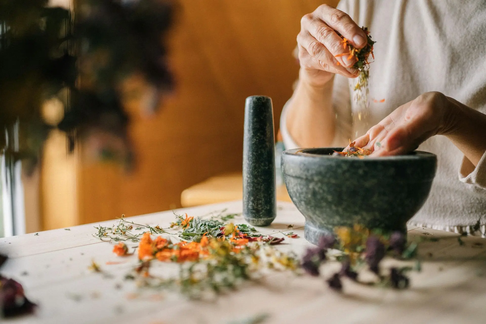 Hands mixing dried flowers in a stone mortar.