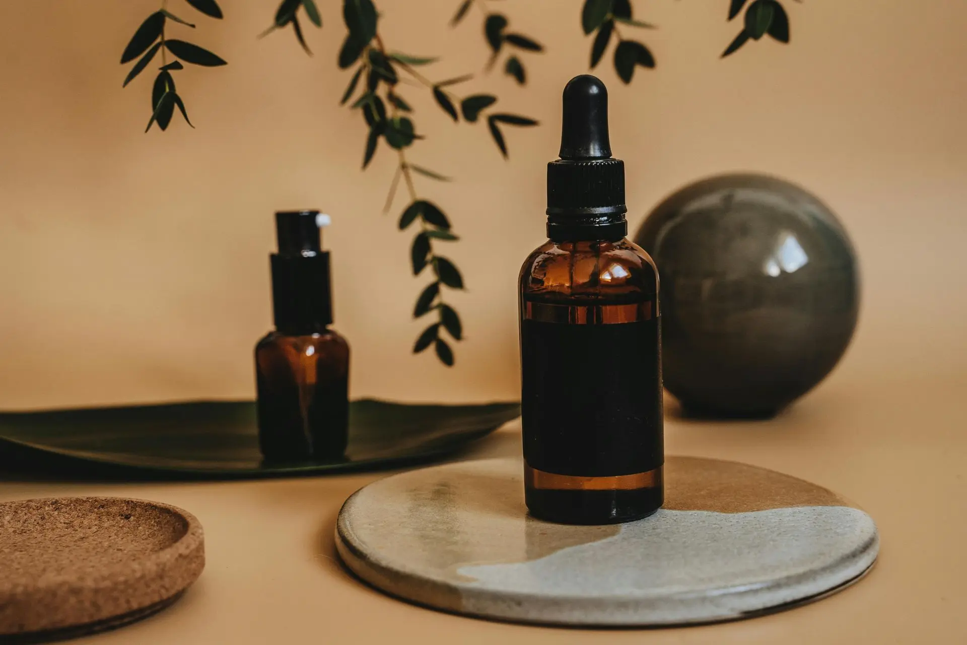 Amber essential oil bottle with dropper on ceramic tray and botanical backdrop.